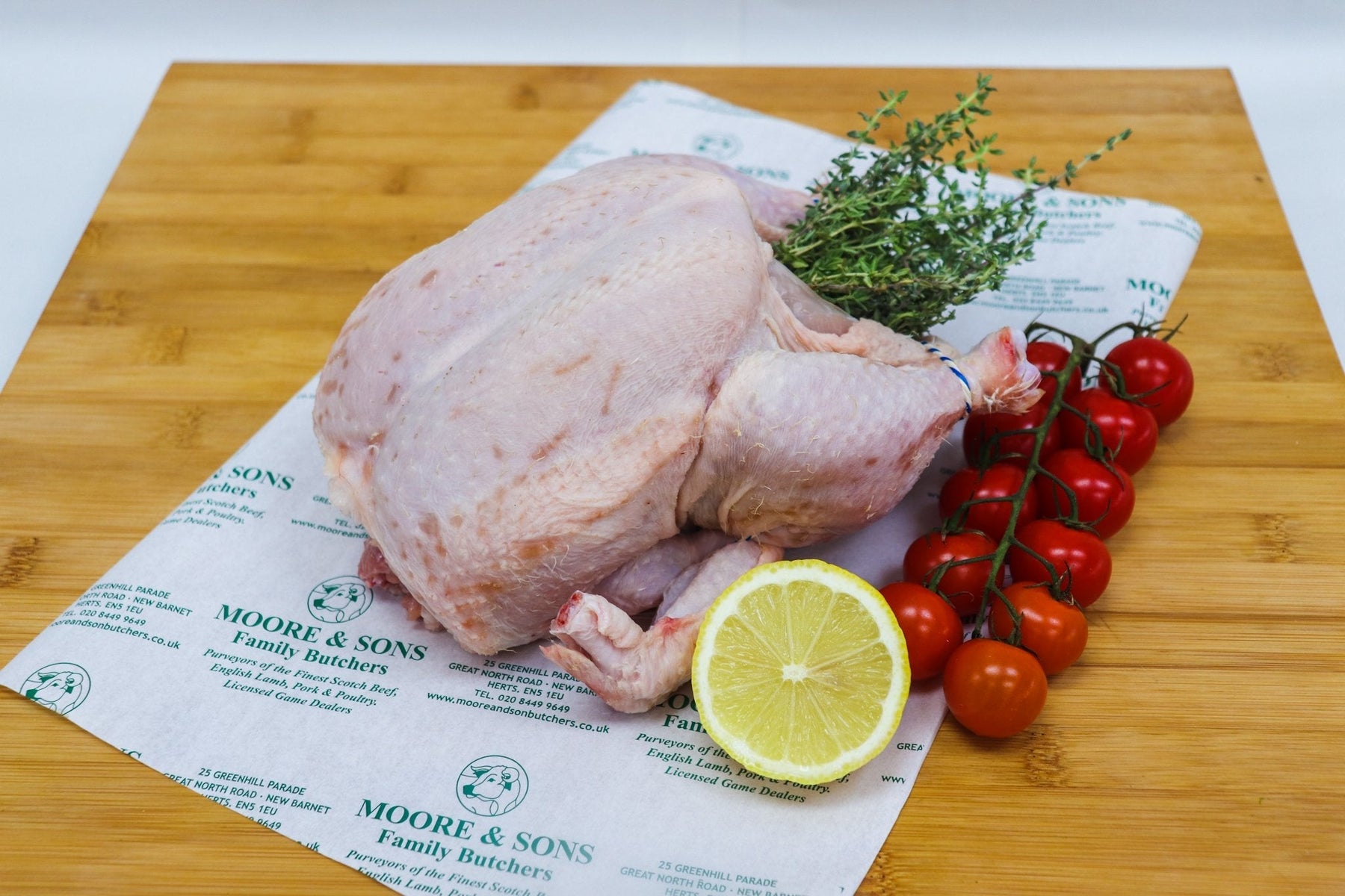 whole chicken on a butcher block with tomatoes, herbs and a lemon on the side