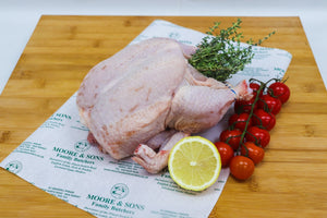 whole chicken on a butcher block with tomatoes, herbs and a lemon on the side